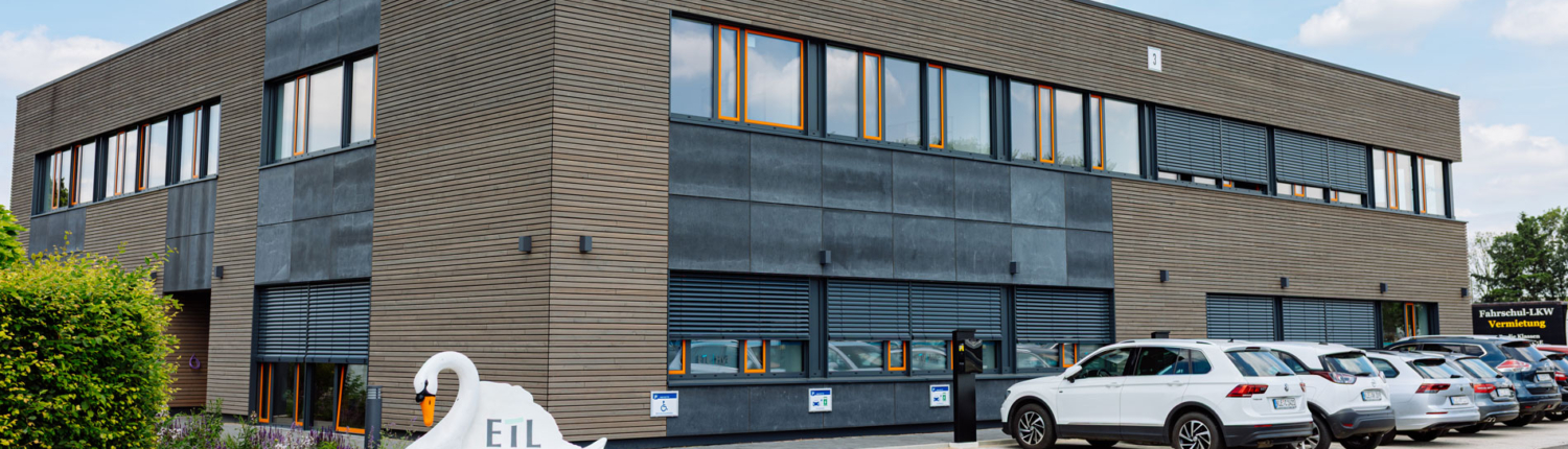 Aussenansicht des Bürogebäudes von ETL in Kleve. Davor stehen parkende Autos und eine Bank in Schwarmform mit dem Logo ETL